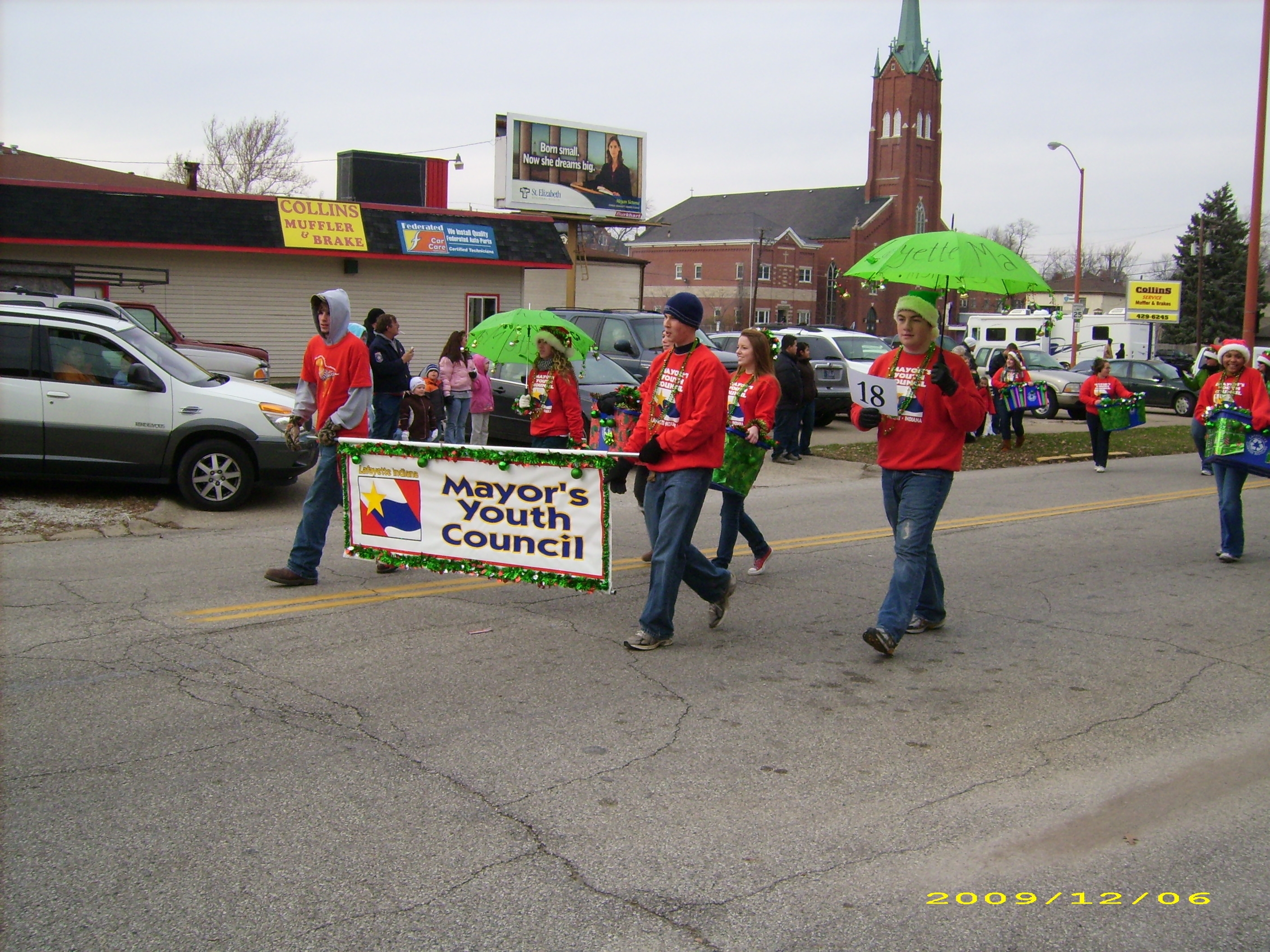 A group of teens in red shirts walking in a parade holding a sign